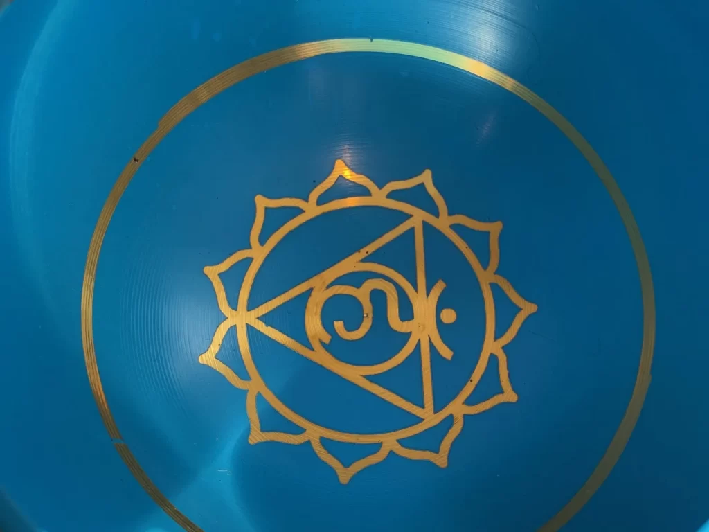 A crystal singing bowl decorated with a gold chakra symbol